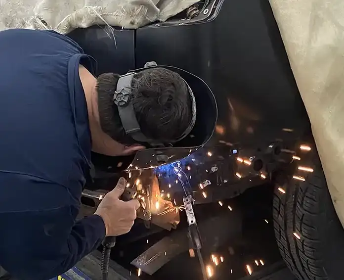 A worker performs a welding job on the body of an automobile.