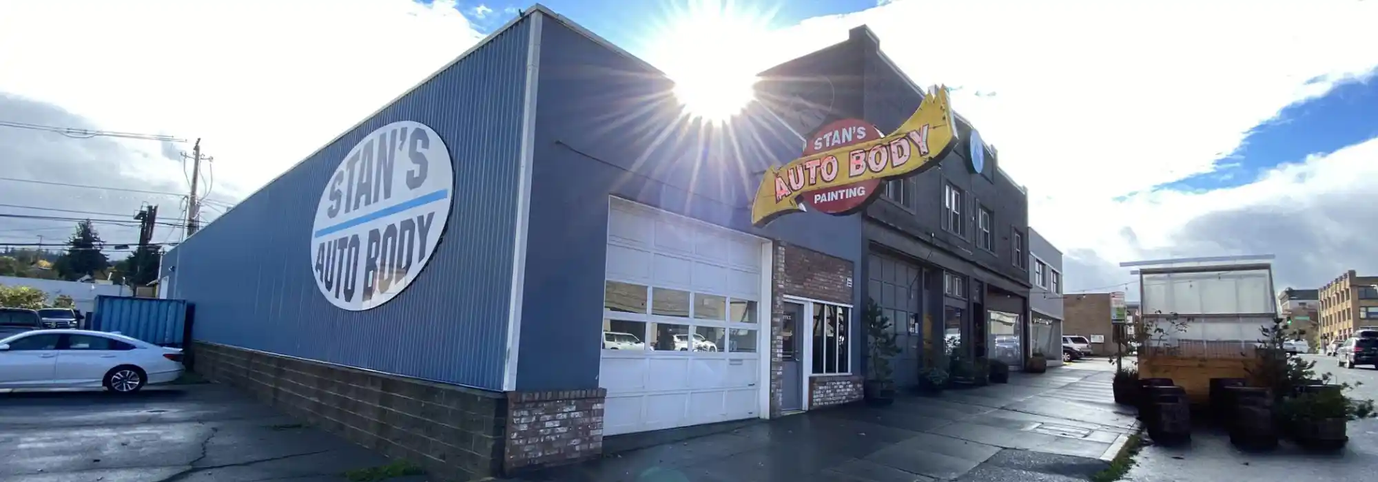 A view of the Stan's Auto Body building. The garage entrance and front door are shown, as well as large signs at the front and sides of the building with the business name on them.
